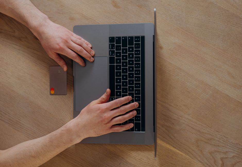 Manos sobre el teclado de un portátil con una tarjeta bancaria al lado, sobre una mesa de madera